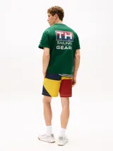 Remera verde de algodón con cuello redondo y corte amplio. Presenta el logo de Tommy Hilfiger en el pecho y un logo oversize en la parte trasera. Tiene mangas cortas con hombros caídos y un parche con logo en la manga.
