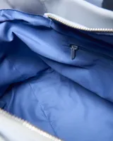 Cartera tipo tote color celeste, con asas de hombro y tiras frontales con la inscripción de la marca en relieve. Cuenta con un pequeño aplique circular con el logo en el centro.