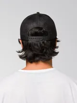 Gorra tipo trucker de color negro con malla posterior y parche frontal circular con el logo de Caterpillar en amarillo y negro. Cuenta con visera curva y cierre ajustable en la parte trasera.