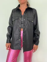 Camisa negra de cuero sintético con textura croco, corte recto, cuello clásico, cierre frontal con botones a presión, dos bolsillos con solapa en el pecho y mangas largas con puños abotonados.