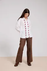 Camisa blanca de corte holgado con cuello camisero y cierre frontal de botones. Presenta un delicado bordado vertical de flores pequeñas en color bordó a lo largo de la botonera y en el cuello.