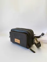 Bandolera de cuero negro con textura grabada tipo cocodrilo en el frente y laterales lisos. Cuenta con doble compartimento con cierre metálico, correa larga ajustable y etiqueta de cuero natural con logo grabado.