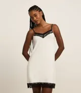 Camisón corto de color blanco, con escote en V adornado con encaje negro y tirantes finos ajustables. El ruedo también está decorado con un borde de encaje negro.