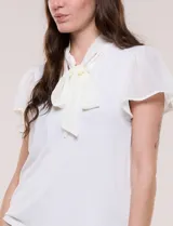 Blusa blanca elegante con cuello con lazo integrado para anudar al frente, escote en V sutil y mangas cortas estilo mariposa de gasa translúcida.