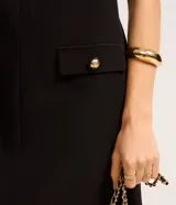 Vestido corto negro de crepé con escote en V tanto en la parte delantera como en la trasera. Tiene bolsillos delanteros con botones dorados.