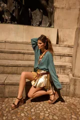 Minifalda de cuero color dorado metalizado con efecto plisado y volados. Presenta un fajón ancho en la cintura con hebilla de estilo rústico.