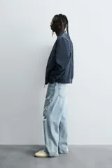 Cazadora bomber ligera de tejido técnico color verde oliva, con cuello, puños y bajo en rib elástico. Presenta cierre frontal de cremallera y bolsillos de vivo en la cadera.