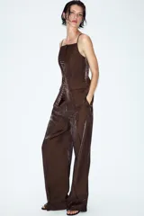 Pantalón de tiro alto color marrón con tejido de efecto brillo y pernera recta. Cuenta con bolsillos delanteros y cierre frontal con cremallera, botón interior y gancho.