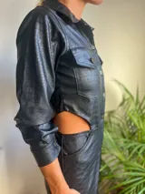Mono corto negro de cuero sintético con textura croco, cuello camisero, cierre frontal con botones dorados, mangas largas con puños abotonados, bolsillos con solapa en el pecho y aberturas laterales en la cintura.