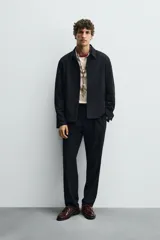 Pantalón negro de corte recto (regular fit) confeccionado en tejido compacto. Presenta pliegues frontales marcados, cierre frontal con botón y cremallera, y bolsillos de vivo en la parte trasera.