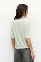 Remera negra de cuello redondo y manga tres cuartos, confeccionada en tela con textura sutil. Presenta fruncidos laterales que aportan caída y movimiento a la prenda.