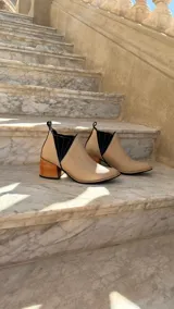 Botinetas de cuero color beige claro con inserciones elásticas laterales en negro y taco cuadrado de madera. Presentan punta fina y tirador trasero.