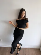 Conjunto de dos piezas en tela bambula elastizada color negro. Incluye un top corto con escote tipo bardot y una falda midi ajustada con tajo lateral.