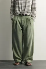 Pantalón chino baggy fit color verde militar, confeccionado en denim de algodón rígido, con corte holgado, tiro medio y pliegues frontales. Presenta bolsillos laterales y cierre frontal con cremallera y botón, con efecto lavado.