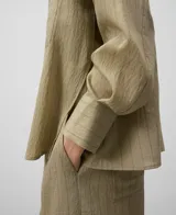 Camisa color verde claro con rayas verticales, cuello bowling, manga larga caída, bolsillo de parche en el pecho, puños abotonados y cierre frontal con botonadura central.