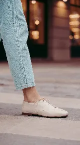 Zapato de cuero marrón chocolate con cordones finos negros, punta cuadrada y detalles de perforaciones decorativas en los laterales.