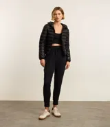 Campera puffer deportiva de mujer, confeccionada en tejido tecnológico ligero con relleno acolchado. Presenta capucha integrada, cierre frontal con cremallera y diseño de manga larga. La prenda destaca por su versatilidad, siendo capaz de transformarse en una pequeña cartera.