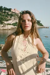 Vestido midi de color beige con escote en pico y tirantes anchos. Presenta un diseño con tejido plisado en la parte superior y aplicaciones de encaje a tono en el escote y la cintura. Cuenta con una tira ajustable con lazada en la espalda y forro interior.