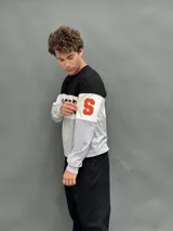 Buzo de cuello redondo con diseño de bloques de color en negro, blanco y gris. Presenta la palabra 'SYRACUSE' estampada en el frente y detalles en naranja en las mangas.