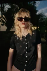 Chaqueta de punto pointelle negra, de manga corta y cuello redondo, con diseño de estrellas y cierre frontal con botones.