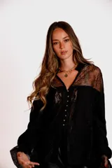Camisa negra de manga larga con detalles de encaje en hombros y puños. Presenta un cuello tipo solapa y cierre frontal con botones dorados.