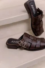 Suecos de cuero vacuno color marrón, marca Amén, con diseño de tiras entrelazadas, puntera cuadrada y hebilla metálica ajustable en el lateral.