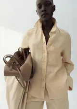 Camisa de lino color beige, de diseño recto con cuello camisero, manga larga con puños abotonados, bolsillo de parche en el pecho y cierre frontal de botones.