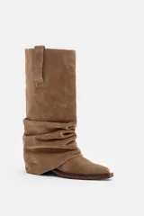 Bota de caña alta confeccionada en gamuza color marrón, con diseño drapeado en la zona del tobillo y taco bajo cuadrado.