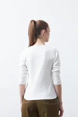 Remera de manga larga color beige, confeccionada en algodón, con escote en V y cartera corta de botones blancos.