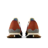 Championes New Balance unisex modelo XC-72, con capellada de gamuza color mostaza, detalles en celeste, bordó y naranja, logo "N" en bordó, entresuela blanca y suela marrón con diseño de tracción agresivo.