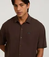 Camisa de corte relajado para hombre, confeccionada en una mezcla de cáñamo y algodón. Presenta cuello inglés, manga corta, cierre frontal con botones y un bolsillo en el pecho con una pequeña etiqueta aplicada.