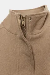 Cazadora corta de paño color tostado, con cuello alto, mangas largas, bolsillos frontales con solapa y cierre con cremallera oculta y botones a presión metálicos.