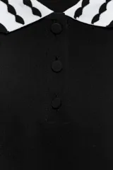 Top de tejido negro con cuello polo y bordes de manga cortos con diseño de ondas en blanco y negro. Tiene un cierre frontal de botones.