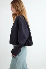 Campera corta oversize de color negro, confeccionada en algodón, con mangas largas, cuello redondo, cierre frontal de botones y bajo con elástico fruncido.