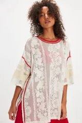 Remera oversize de inspiración deportiva en malla de encaje color blanco, con terminaciones en rojo, franjas estilo varsity en las mangas, escote redondo, hombros caídos y aberturas laterales en el ruedo.
