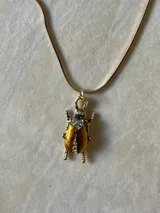 Collar de cadena fina dorada con dije en forma de escarabajo, con acabado texturizado y detalles de cristales incrustados.