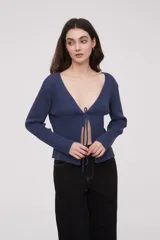 Saco de punto acanalado color azul, con escote profundo en V y cierre frontal mediante lazo para anudar. Presenta mangas largas y diseño holgado.
