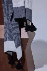 Chal de lana con diseño de patrón paisley y detalles de tejido en punto. Presenta terminaciones con pompones en los extremos.