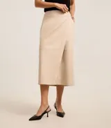 Falda midi negra de cuero sintético con diseño cruzado tipo sobre, bolsillos laterales y cierre trasero.