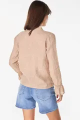 Blusa de lino italiano color beige con escote en V y detalles de volados en el cuello y los puños. Presenta cierre frontal con botones de nácar y mangas largas.