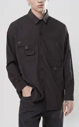 Camisa de manga larga color negro, estilo técnica con calce oversize. Presenta múltiples bolsillos frontales con solapa y detalle de tiras, un pequeño bordado de tijeras en el pecho izquierdo y botones en la cartera frontal y puños.