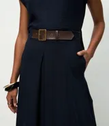 Pollera midi de corte fluido confeccionada en crepé, con pliegues delanteros y cinturón decorativo integrado con hebilla cuadrada. Presenta un diseño minimalista y elegante con cierre discreto.