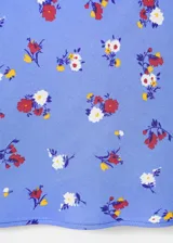 Falda corta de tiro bajo confeccionada en viscosa, con diseño estampado de flores en tonos rojos y blancos sobre base celeste, corte recto con bajo ligeramente acampanado y forro de poliéster.