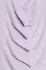 Top de punto sin mangas, color lila, con cuello redondo y diseño de frunces en la parte delantera. Presenta cierre frontal con botones y bajo con abertura.