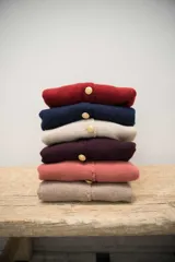 Cardigan de punto color beige con cuello redondo, cierre frontal con botones dorados, bolsillos frontales y terminaciones en crochet. Presenta hombreras internas y diseño de corte recto.