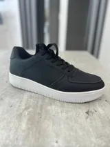 Championes urbanos de estilo clásico, confeccionados en material símil cuero color negro, con suela de goma blanca y cierre mediante cordones.