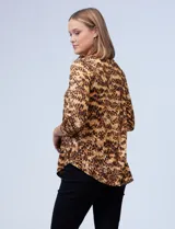 Blusa de seda fría con estampado animal print en tonos marrones. Tiene cuello redondo con escote en V y aro metálico decorativo.