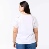 Remera blanca con cuello en V y mangas cortas adornadas con detalles bordados tipo broderie y perforaciones geométricas.