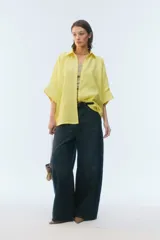 Camisa oversize blanca de lino, con corte cuadrado, mangas raglán cortas con puños anchos, aberturas laterales y cierre frontal de botones.