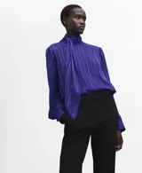 Blusa de manga larga en color azul eléctrico con diseño de rayas verticales sutiles. Presenta un cuello alto con detalle de lazo integrado y cierre frontal con botones ocultos. El tejido es semitransparente con acabado satinado.